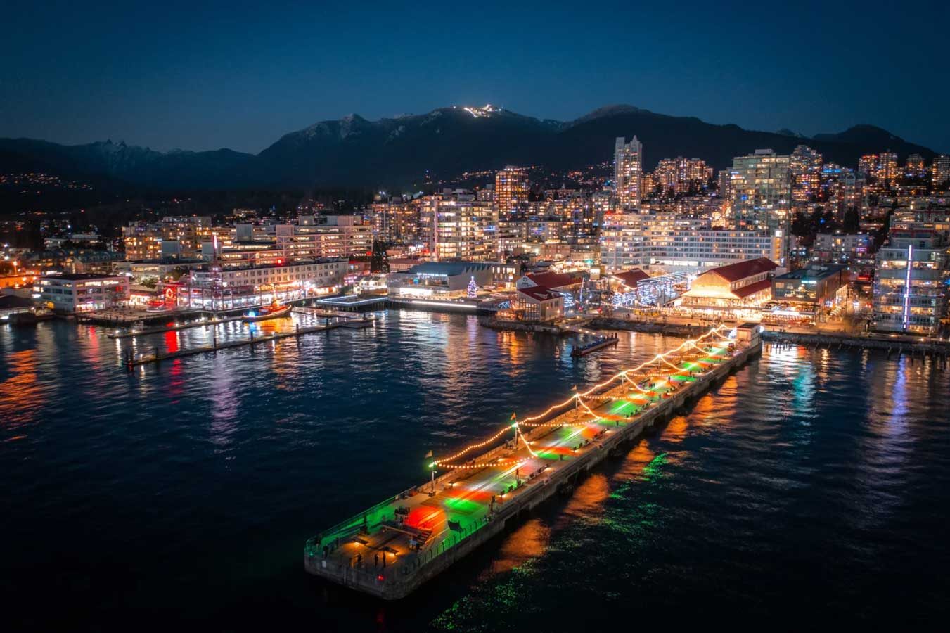 Aerial night view of the Shipyards and North Vancouver waterfront, city lights reflecting on the water