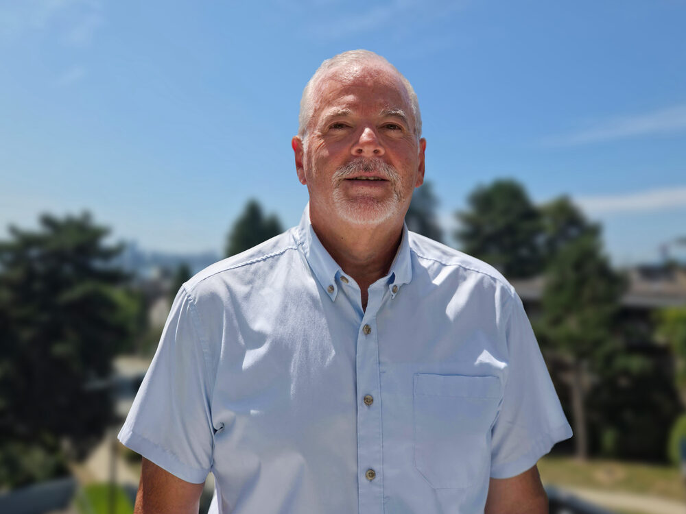 Mike McGraw outdoors in North Vancouver, blue sky and trees behind him