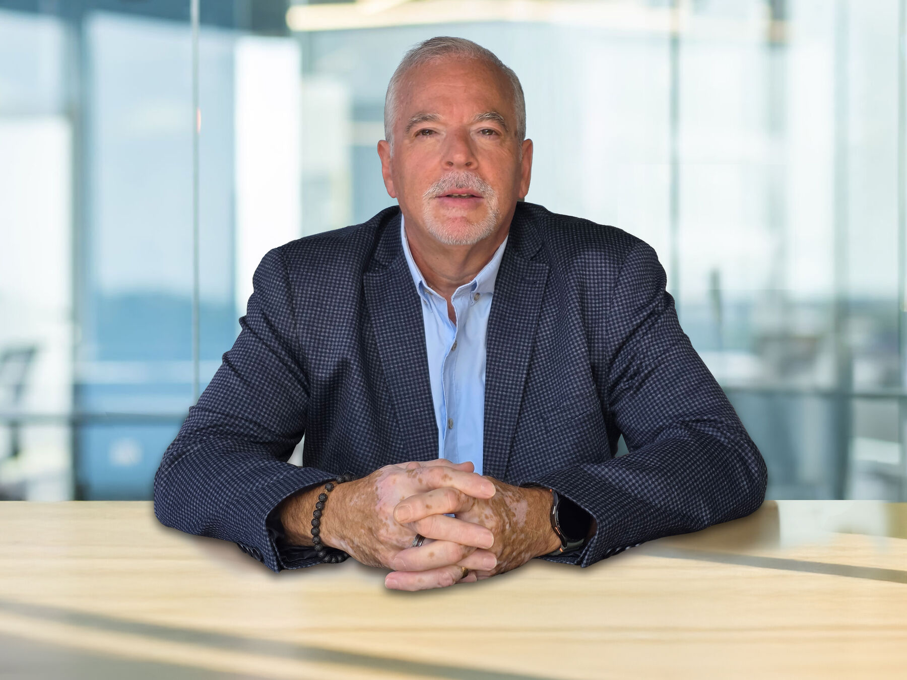Mike McGraw seated at a table, hands clasped, blurred office windows behind him